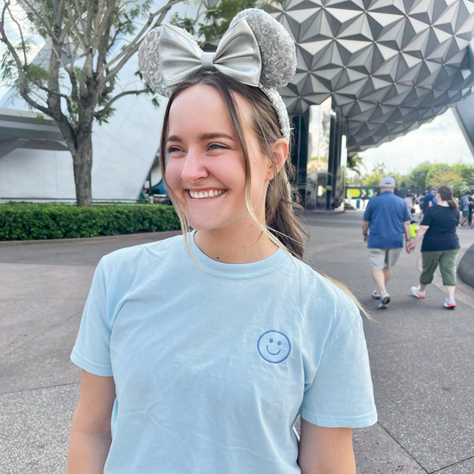 young woman wearing a chambray comfort colors tee with embroidered smiley face in periwinkle thread on the left chest
