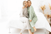 Two women sit on a bed embracing each other in loungewear 