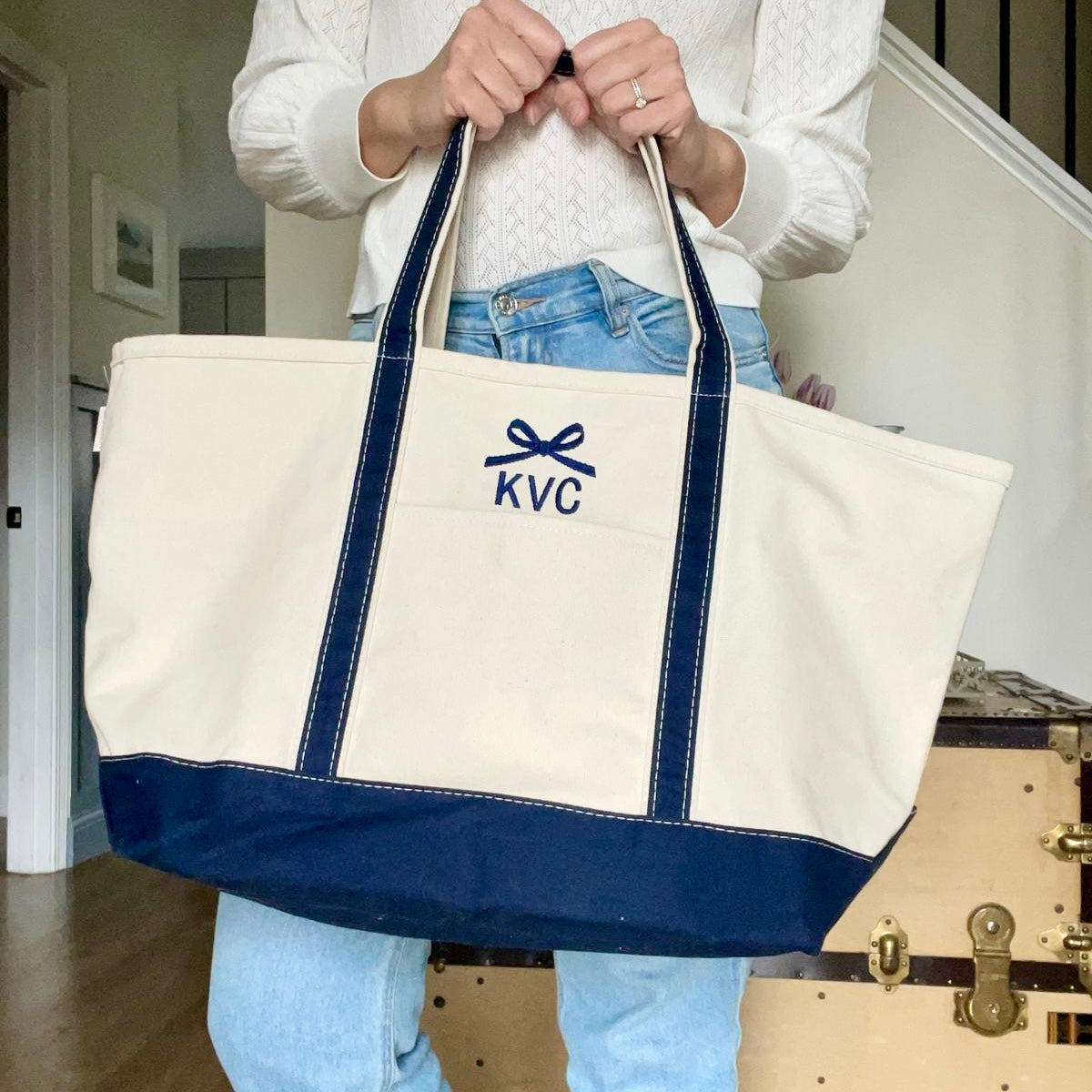 woman holding a natural canvas tote bag with navy trim and custom bow and initial embroidered design