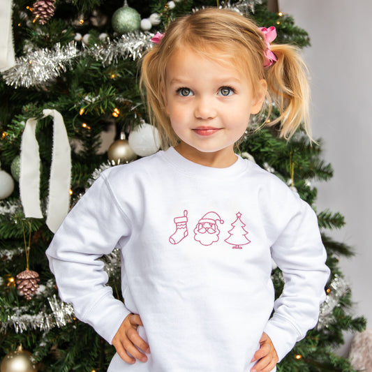 toddler girl wearing a white crewneck with embroidered Christmas icons across the chest in pink thread