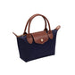 A navy blue canvas handbag with brown leather handles, trim, and a front flap secured by a gold-tone snap button, shown on a plain white background.