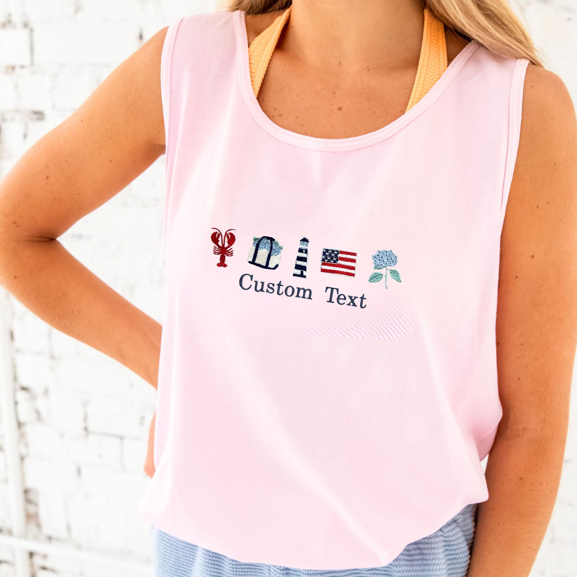 Pink tank top with embroidered designs and text on a blurred white background