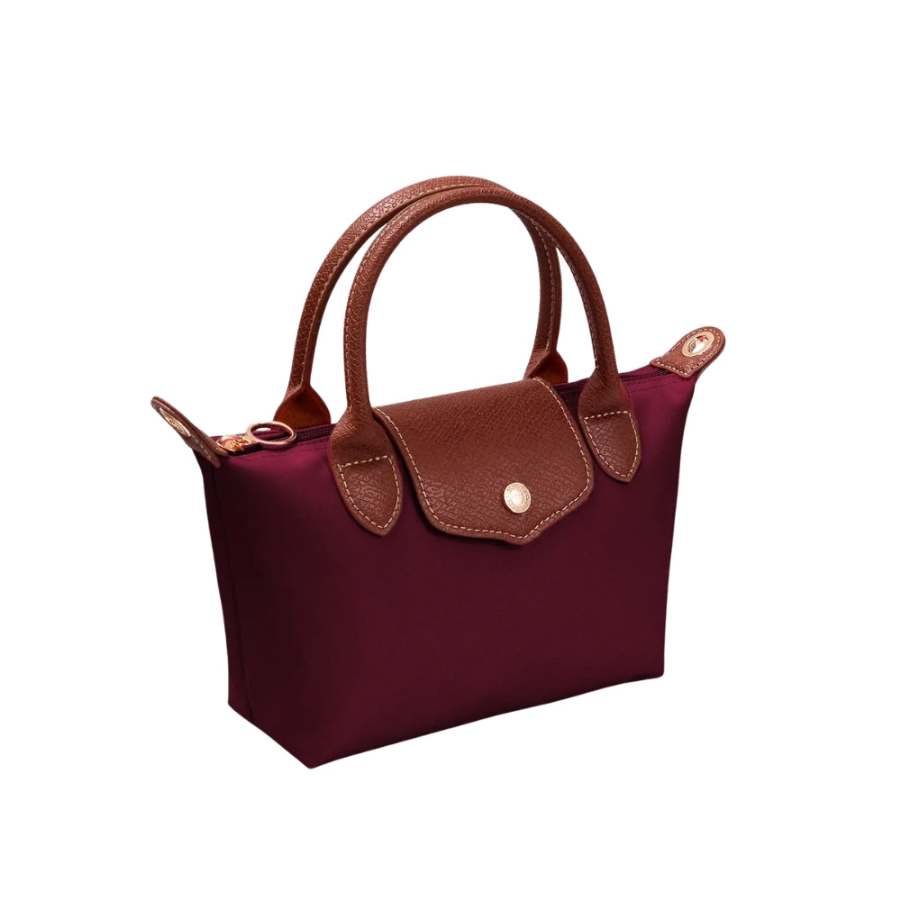 A structured mini handbag in deep burgundy nylon with brown pebbled leather handles, trim, and a front flap closure featuring a gold-tone snap button, shown on a plain white background.
