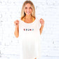 Woman wearing a white t-shirt with small icons and text against a white brick wall.