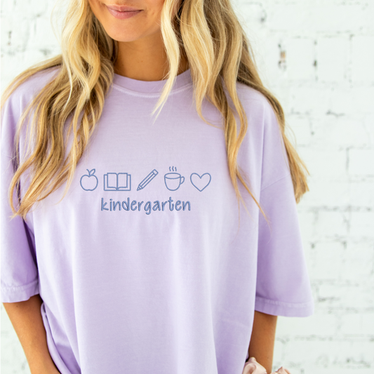 young woman wearing a lilac comfort colros t-shirt with embroidered teacher icons  in periwinkle thread across the chest and custom text underneith