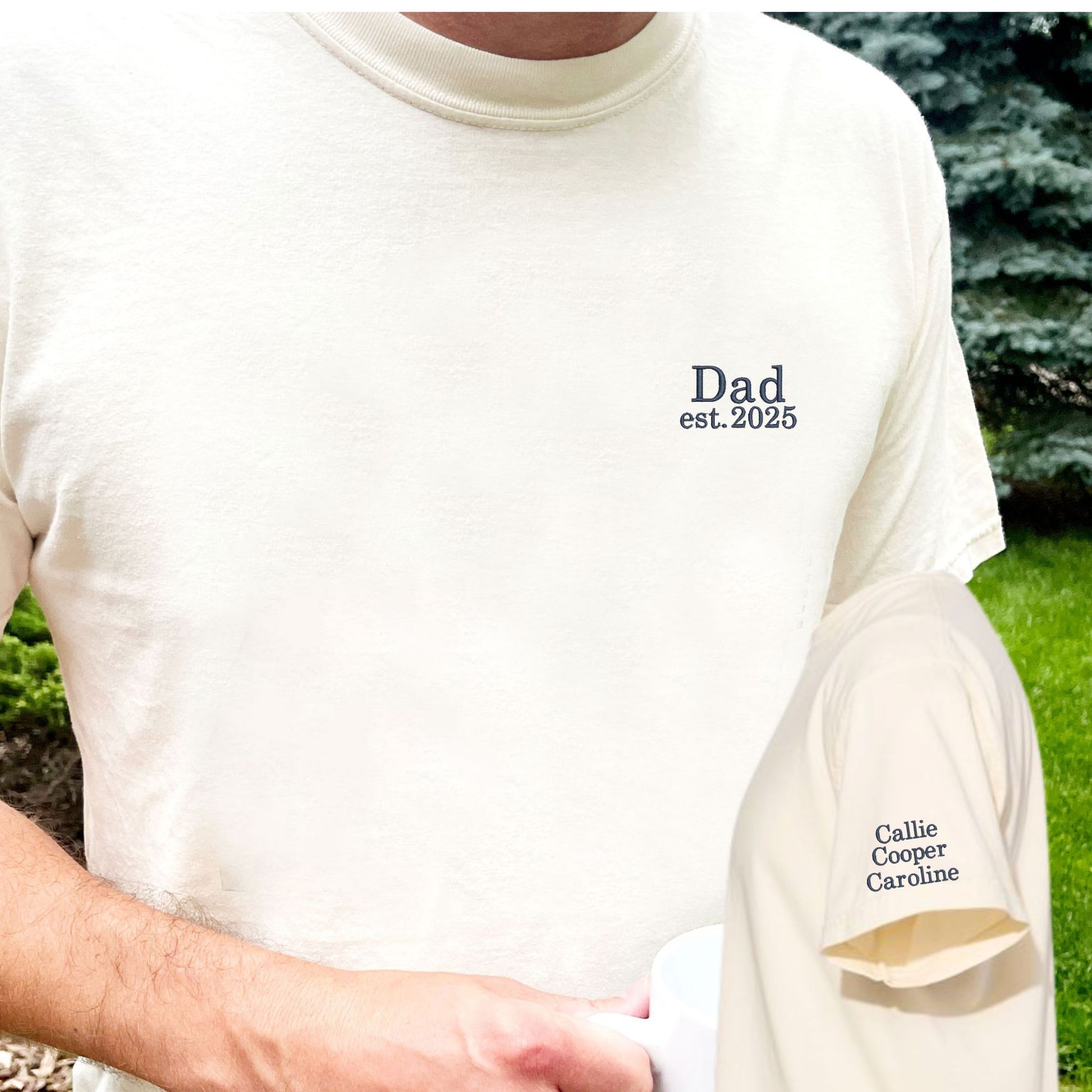 man wearing a large ivory comfort colors t-shirt with minimal dad and date embroidery on the left chest and three kids' names embroidered on the left sleeve in navy thread