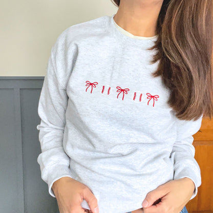Person wearing a light gray sweatshirt with red bow and baseball patterns