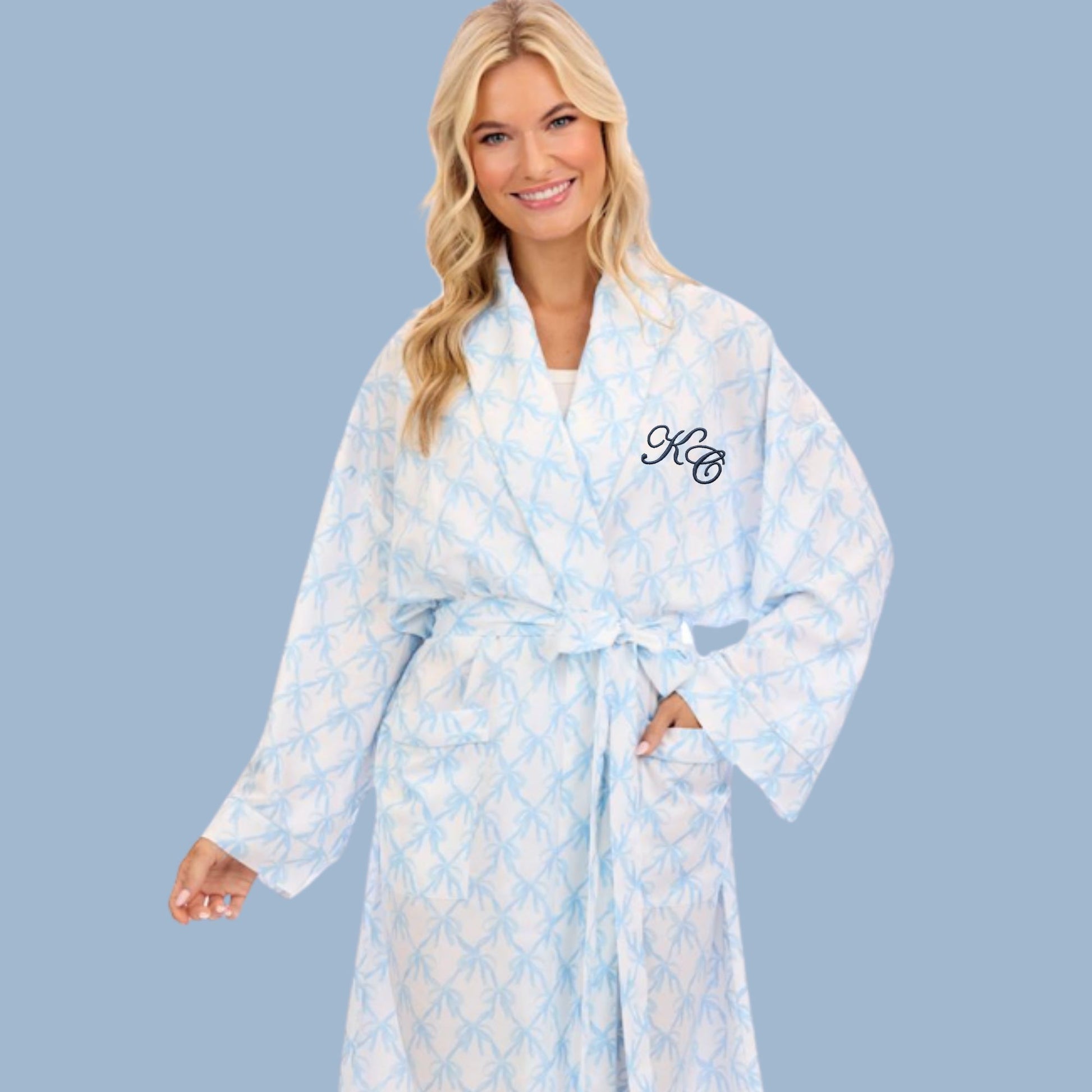 Woman wearing a white robe with a light blue bow pattern with monogram on a solid background