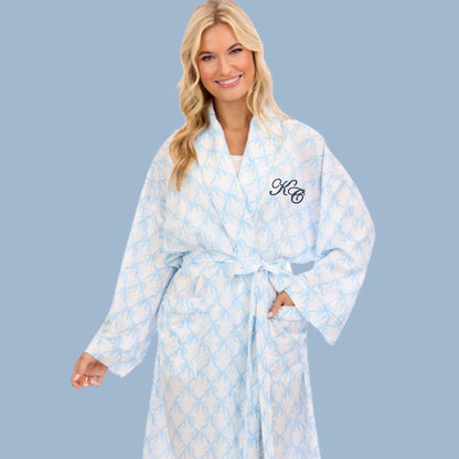 Woman wearing a white robe with a light blue bow pattern with monogram on a solid background
