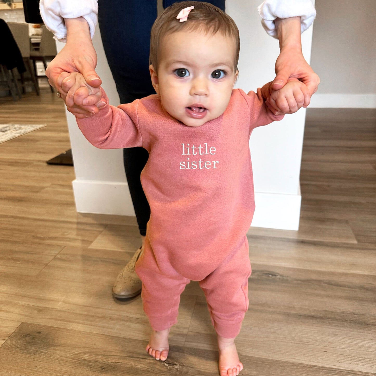 baby wearing a mauve fleece romper with embroidered little sister in white thread on the chest