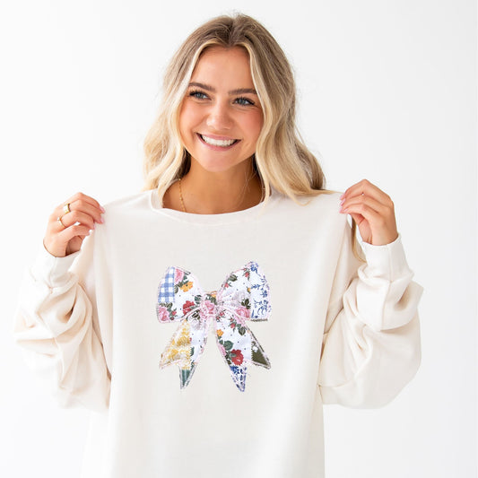 woman wearing a sweet cream crewneck sweatshirt with a custom embroidered bow with vintage inspired patchwork quilted colorful printed fabric