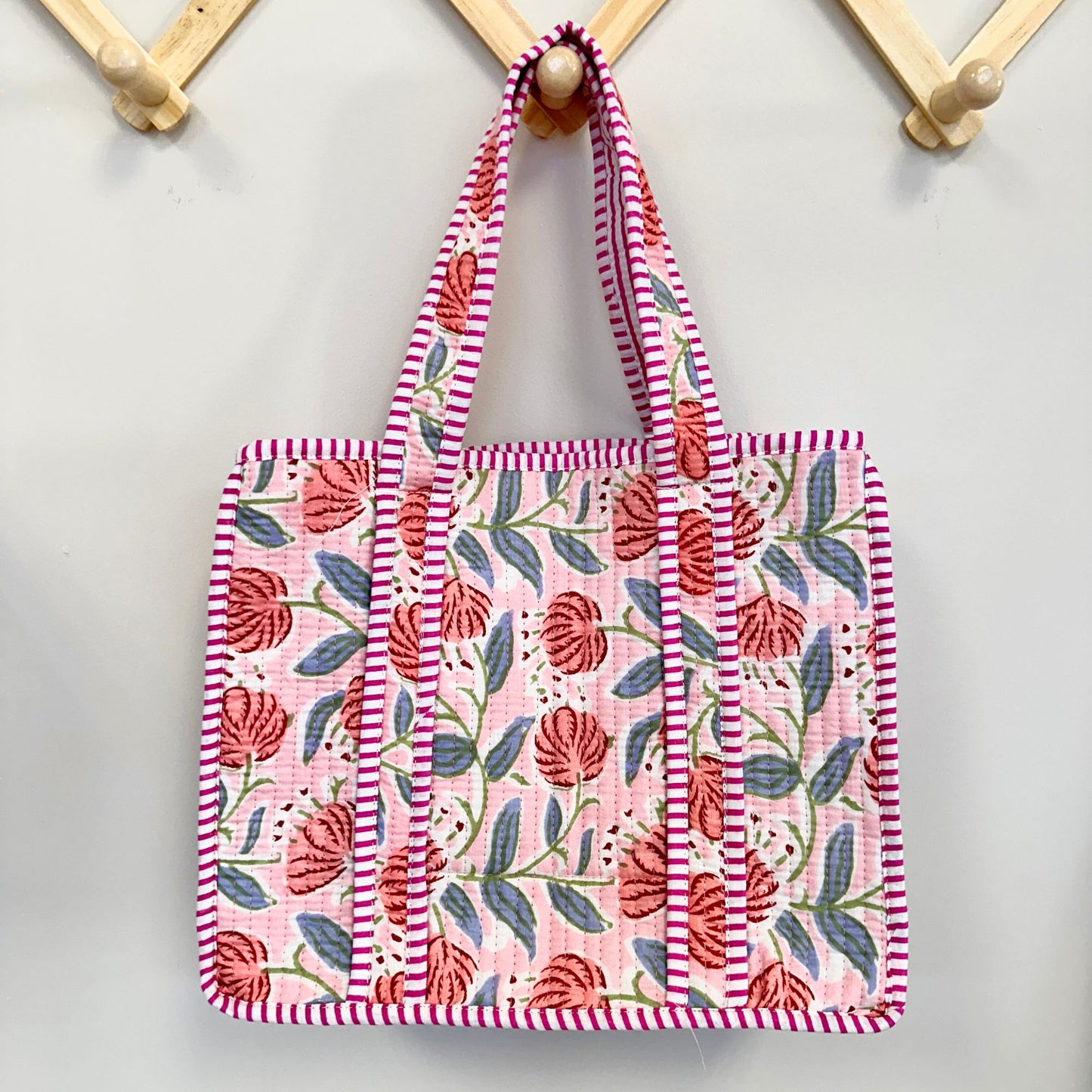 Floral patterned tote bag with striped handles hanging on a wooden hook.