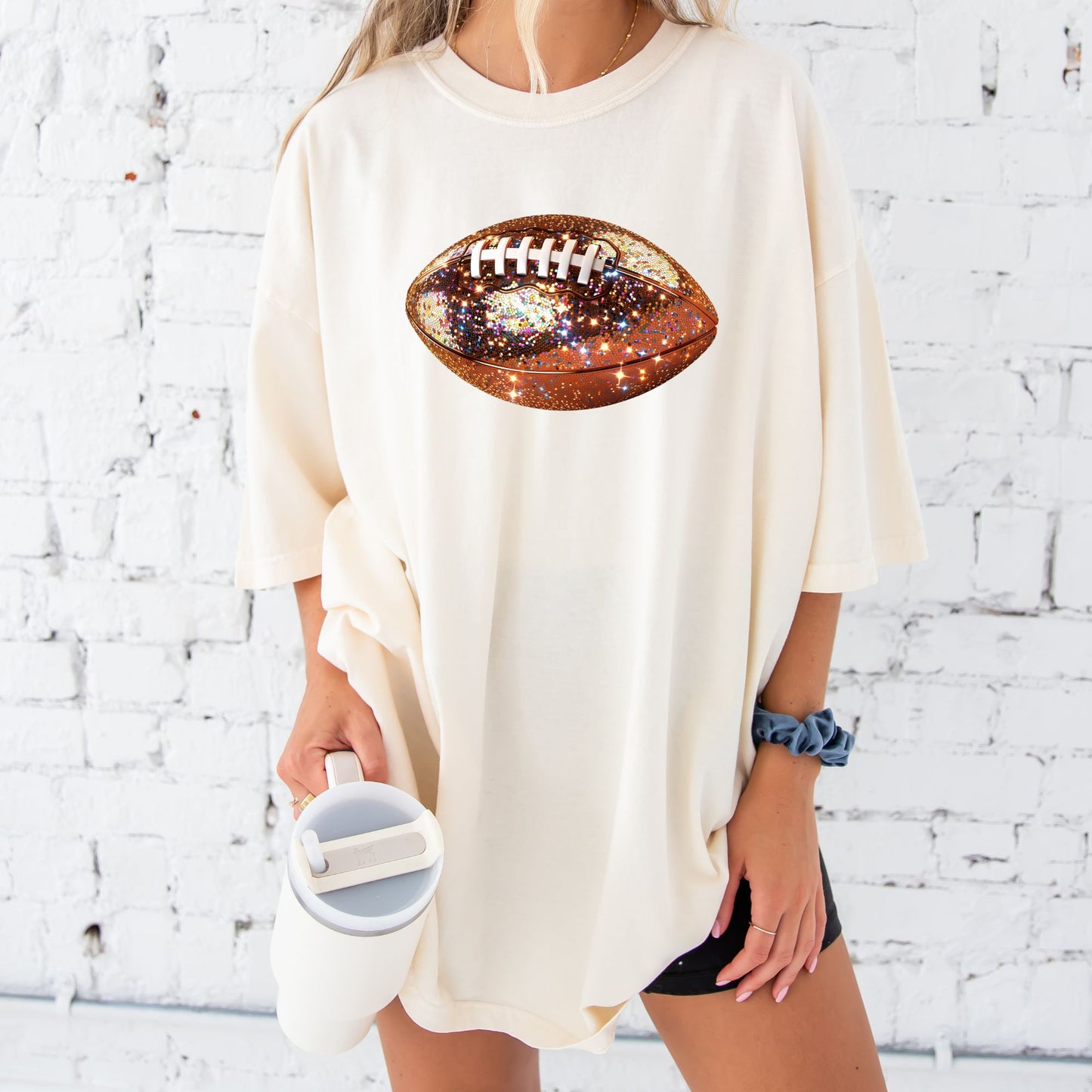 young woman wearing an oversized ivory comfort colors tee with large glitter football print across the front chest