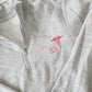 a light heather grey quarter zip with pockets featuring a custom name, credentials, and caduceus embroidered design in shades of pink on the left chest