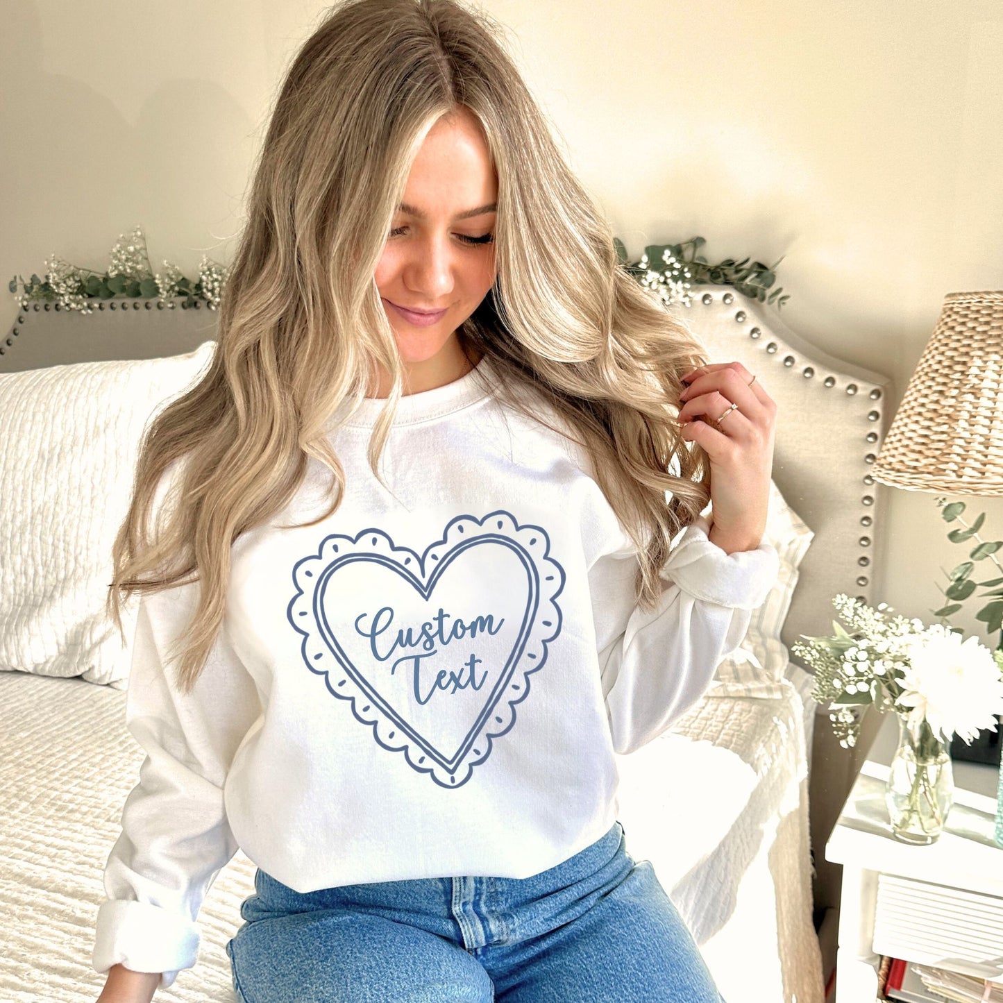 Woman wearing a white sweatshirt with a heart-shaped 'Custom Text' design in a cozy indoor setting.