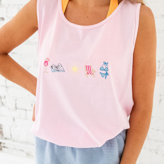 Woman wearing blossom tank with summer drink, book, sun, folding chair, and swimsuit embroidered across the chest. partnered with chambray blue shorts