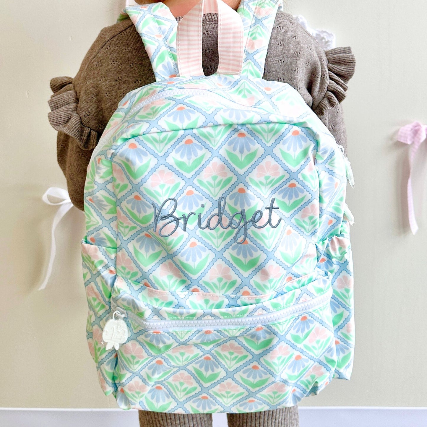 Backpack with pastel floral pattern and 'Bridget' embroidery, worn by a person.