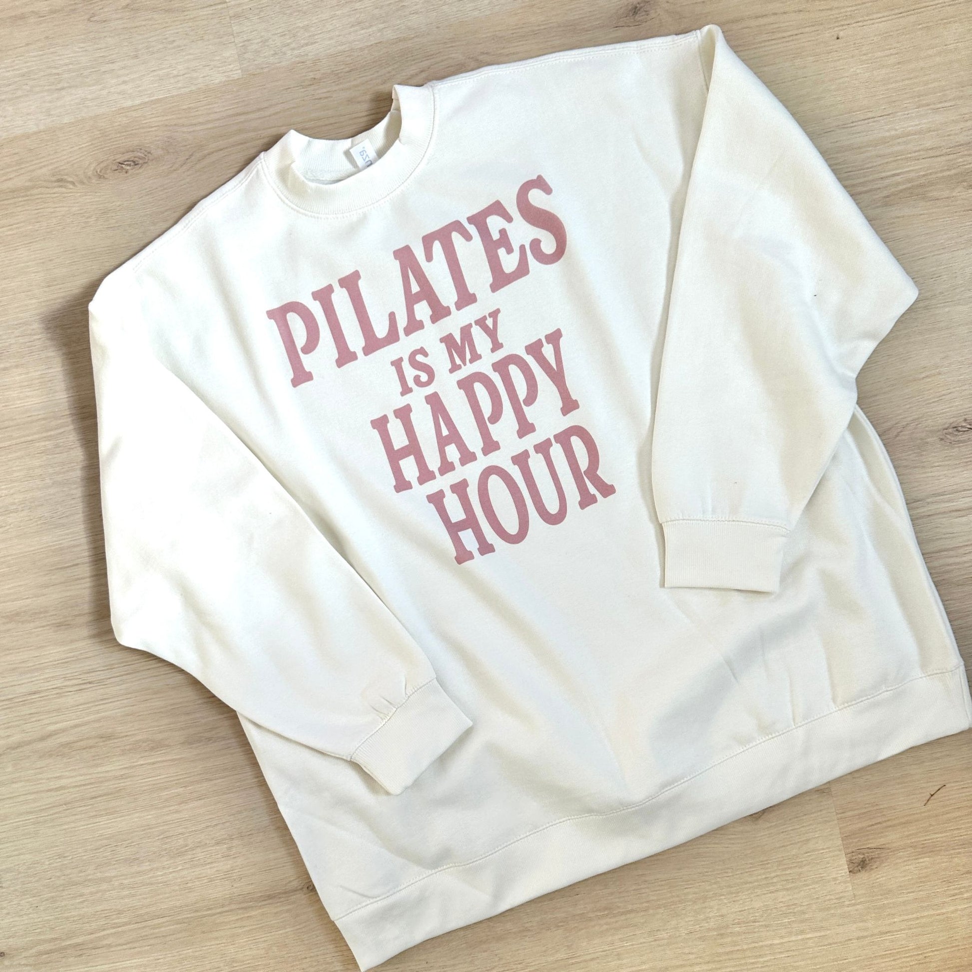 White sweatshirt with 'Pilates is my happy hour' text on a wooden surface