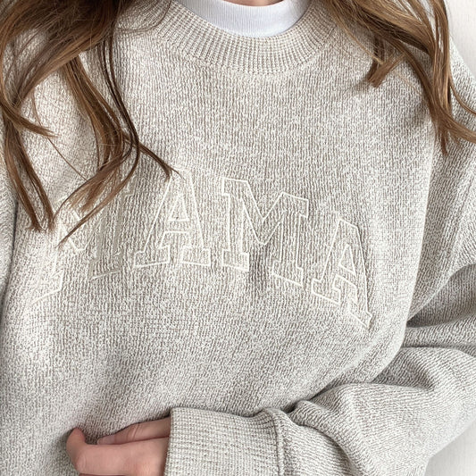 Woman wearing a knit pullover crewneck sweatshirt with a custom mama athletic block embroidered design in a natural thread