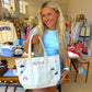 Woman holding a white tote bag with embroidered designs and 'Olivia' in a store setting.