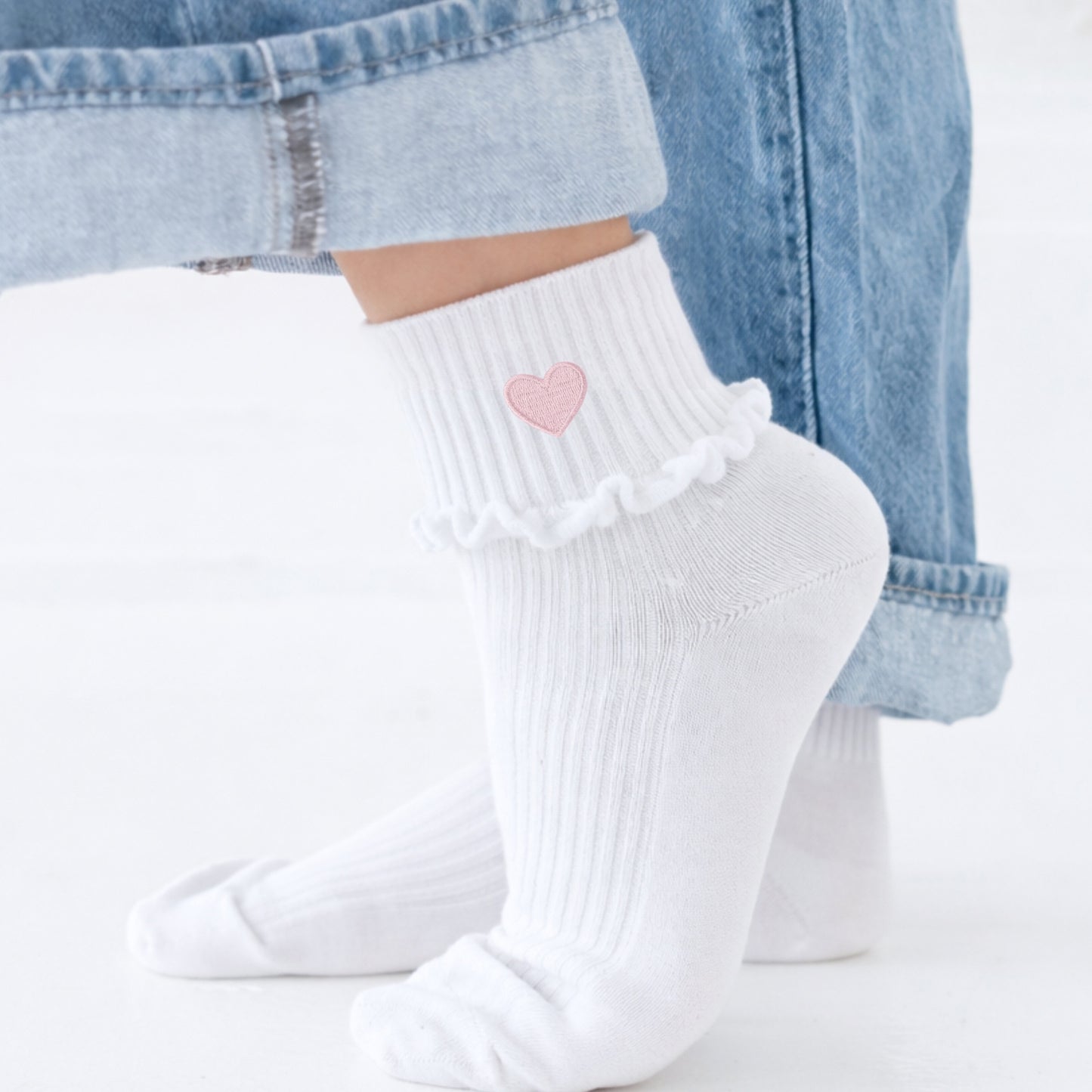 White socks with a pink heart design worn with light blue jeans.