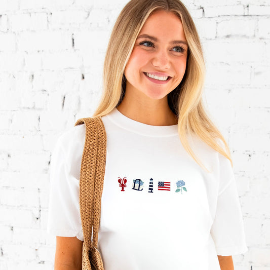 Woman wearing a white t-shirt with embroidered designs against a white brick wall.