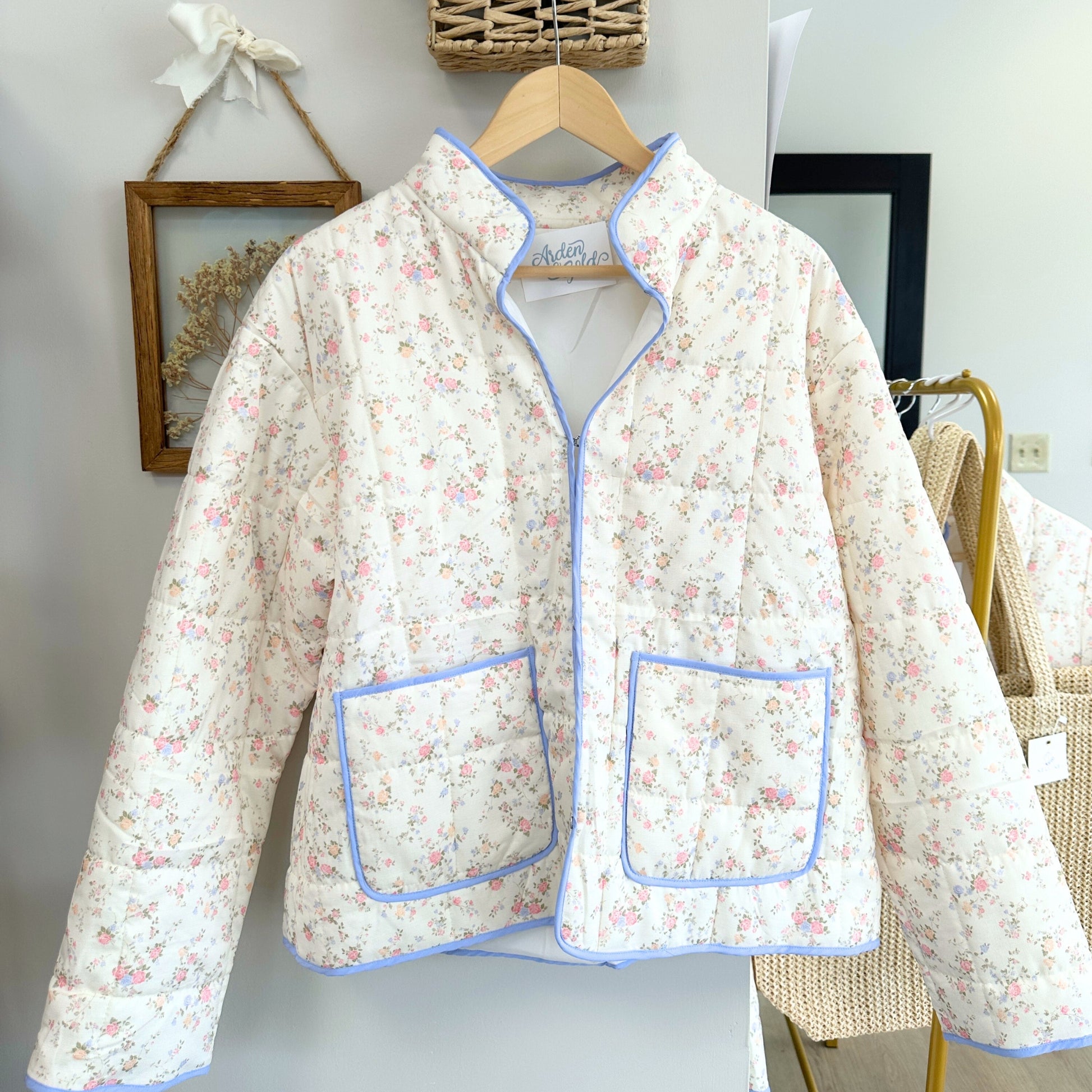 Floral patterned jacket with blue trim on a hanger against a neutral background