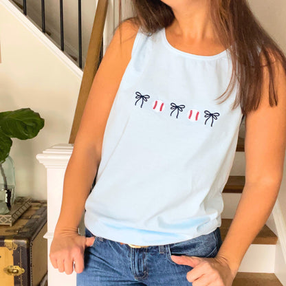 Person wearing a light blue tank top with baseball and bow icons embroidered across the chest in a home setting