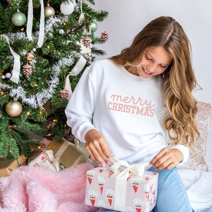 young girl wearing a white crewneck sweatshirt with a custom soft pink merry Christmas print