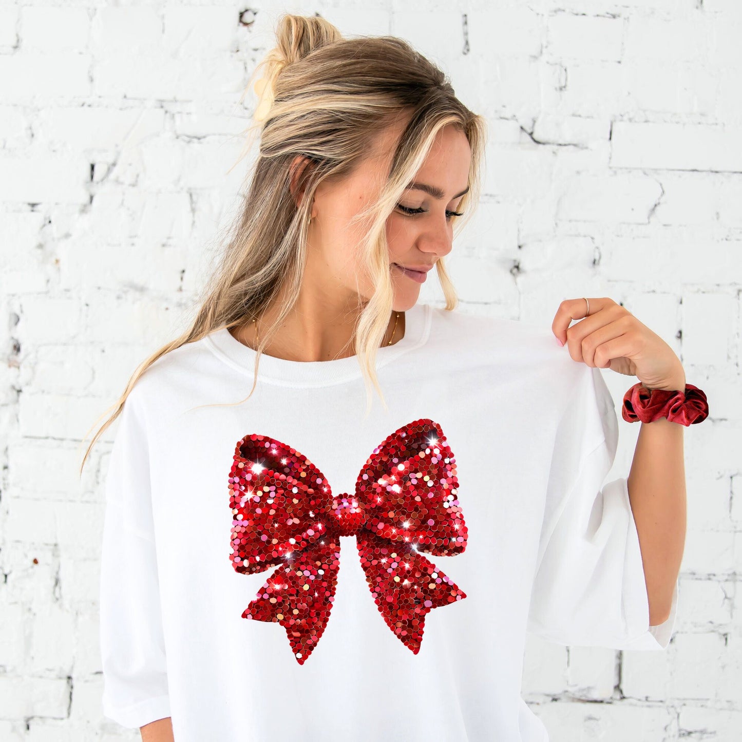 young woman wearing a white comfort colors t-shirt with large printed glitter red bow across the front of the tee