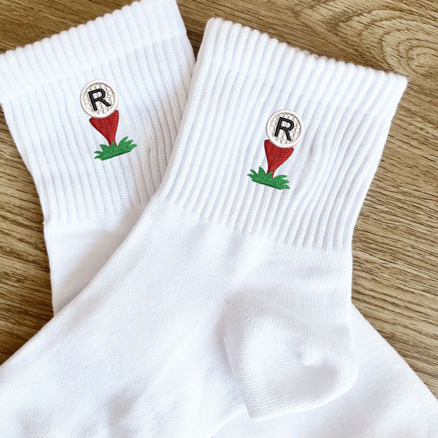 white crew socks with custom golf ball and tee embroidered icon with single letter monogram embroidered on top of the golf ball.