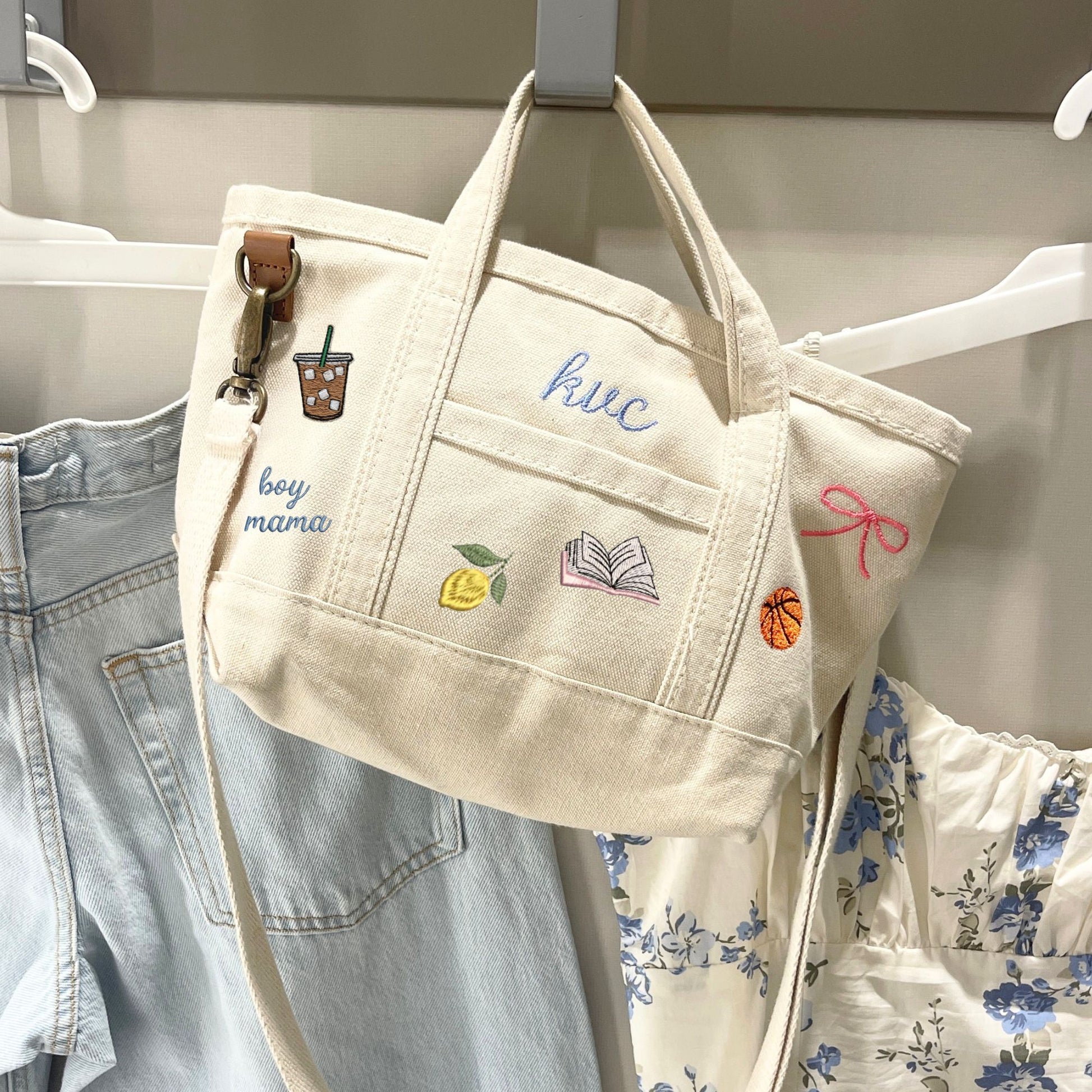 Beige tote bag with embroidered designs hanging on a rack with clothes.