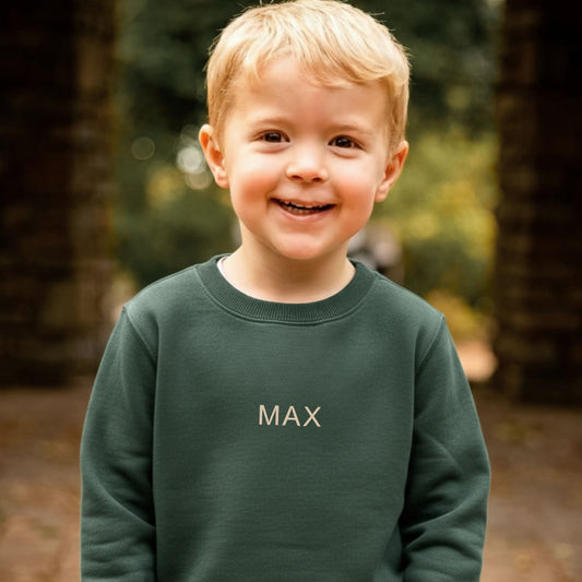 Child wearing a green sweatshirt with 'MAX' on it, standing outdoors.