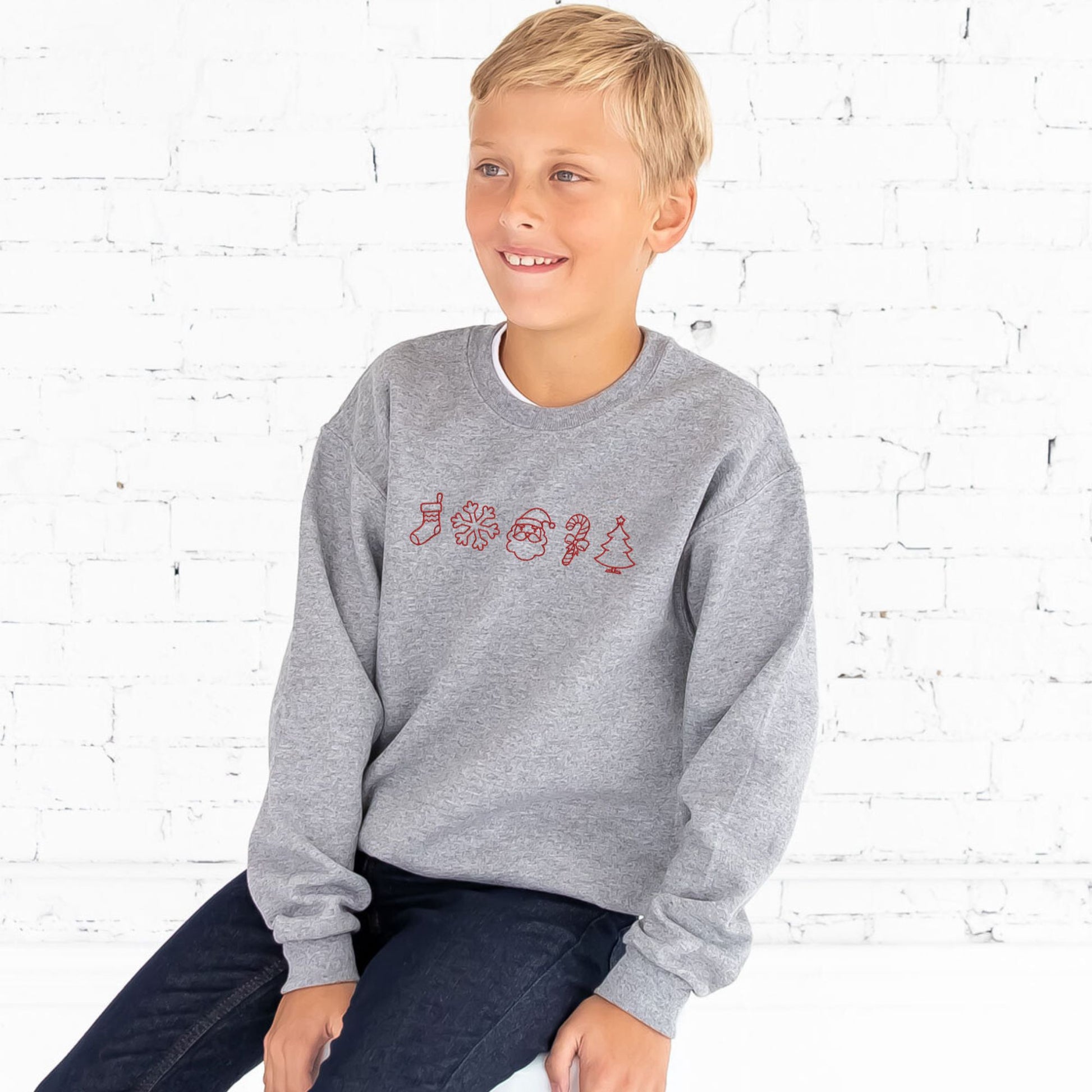 young boy wearing a youth athletic heather crewneck sweatshirt with embroidered charismas icons across the chest in red thread