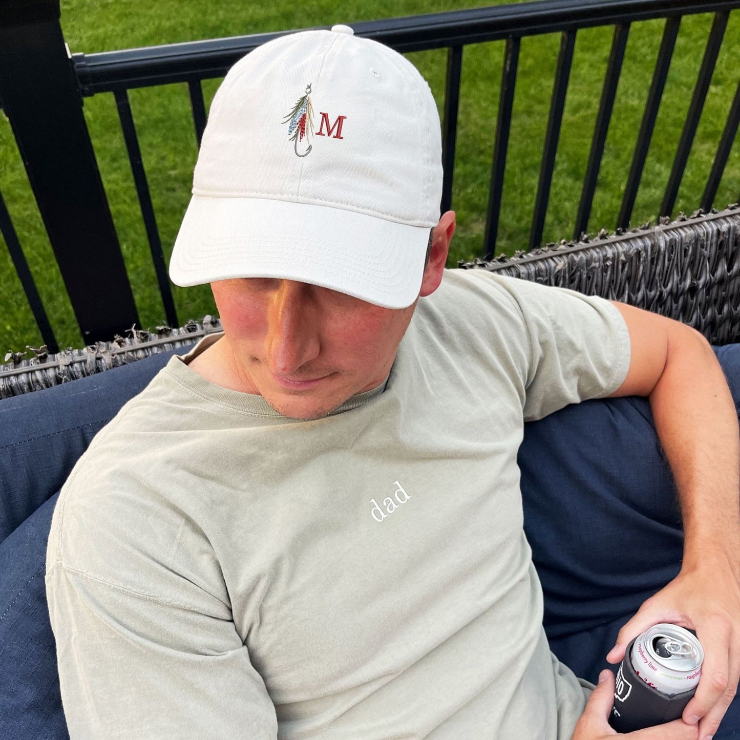 man sitting outside wearing a stone baseball cap with a fly fishing lure and single initial embroidered design on the center front