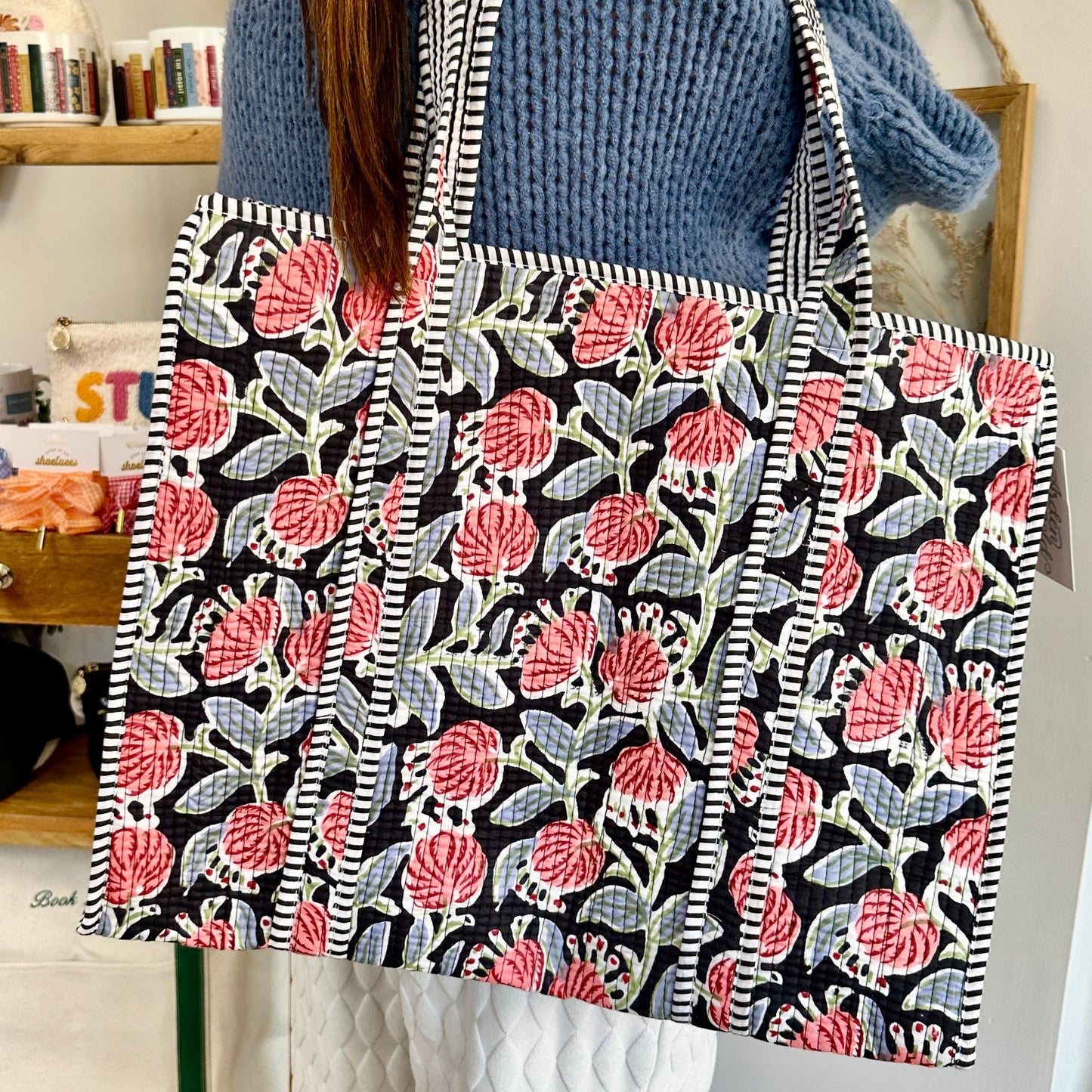 Floral patterned tote bag held by a person wearing a blue sweater.
