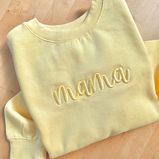 Yellow sweatshirt with 'mama' embroidery on a wooden surface
