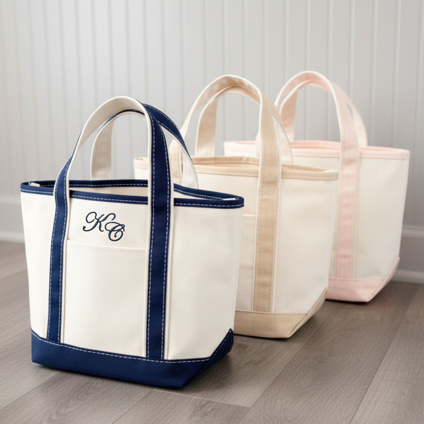 Three tote bags with different color combinations on a wooden floor. front bag embroidered with two initials in an edwardian script font