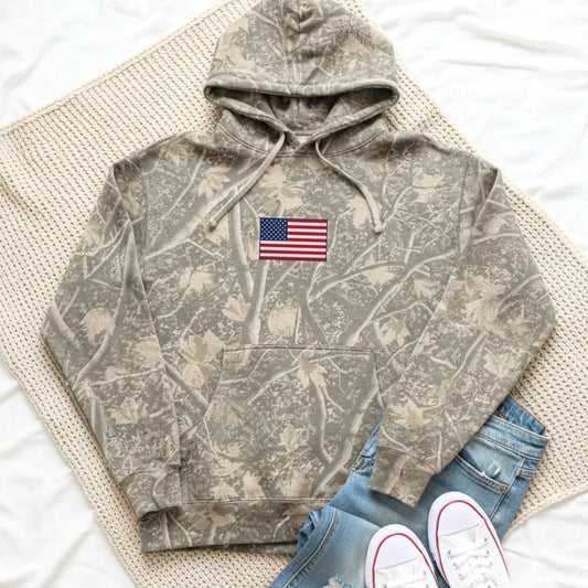 Camouflage hoodie with American flag patch on a textured surface