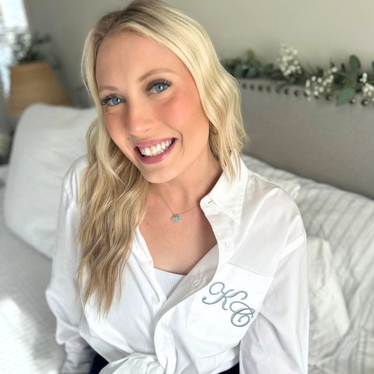 Woman wearing a white button up shirt with monogrammed Edwardian script initials on the pocket  in a home setting