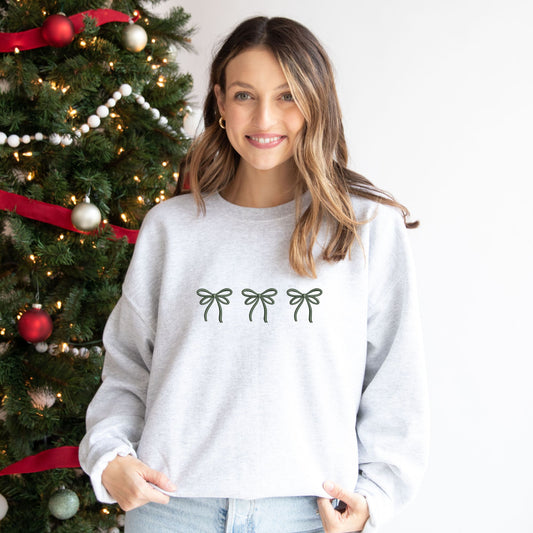 woman wearing an ash crewneck sweatshirt with embroidered three bows cross the chest in ivy thread. 