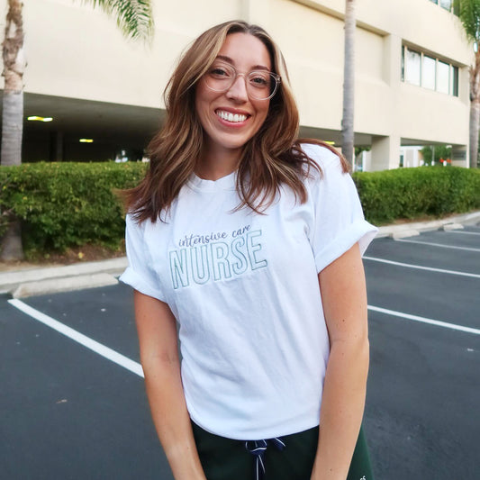 nurse wearing green figs scrub pants and a white comfort colors t-shirt with a custom intensive care nurse embroidered design in gray and eucalyptus