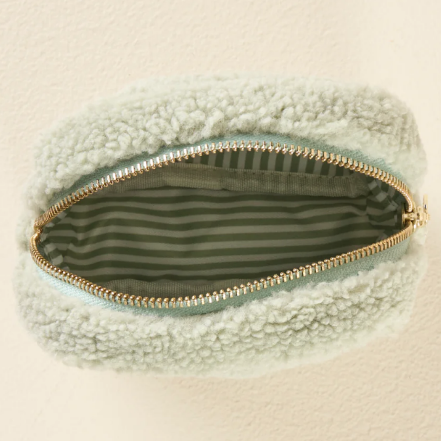 Light green sherpa pouch with gold zipper on a beige background