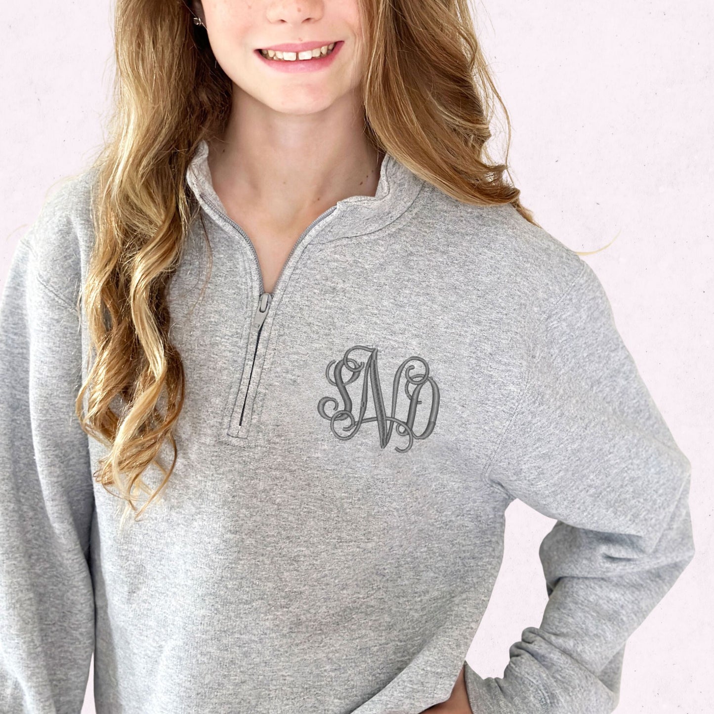 girl wearing an athletic heather quarter zip sweatshirt with a custom embroidered monogram in a gray thread