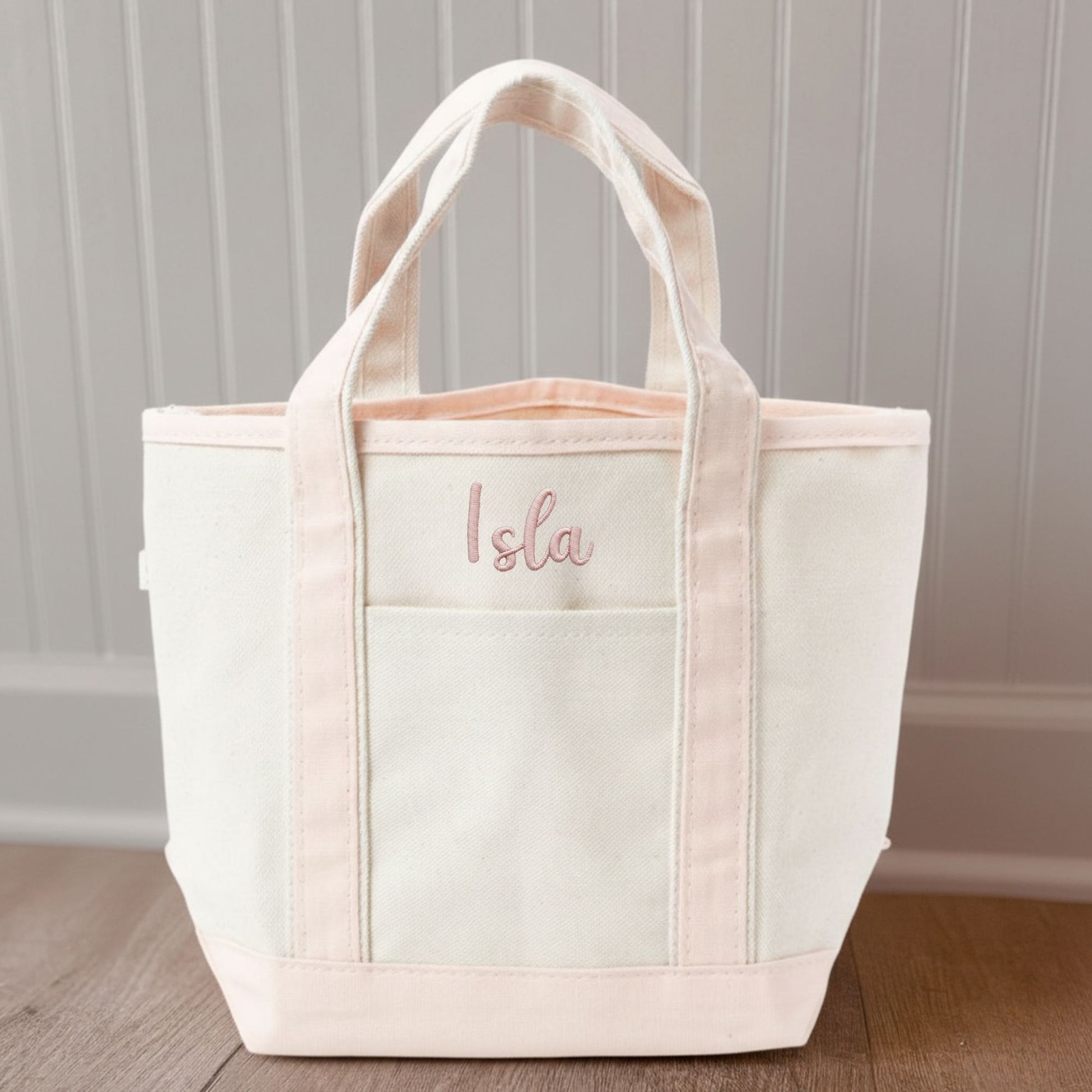 Canvas  tote bag with pink trim and 'Isla' embroidery on a wooden floor.