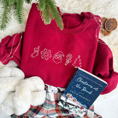 Christmas styled flat lay photo of a cardinal red crewneck sweatshirt with christmas outlined icons embroidered across the chest in white thread.