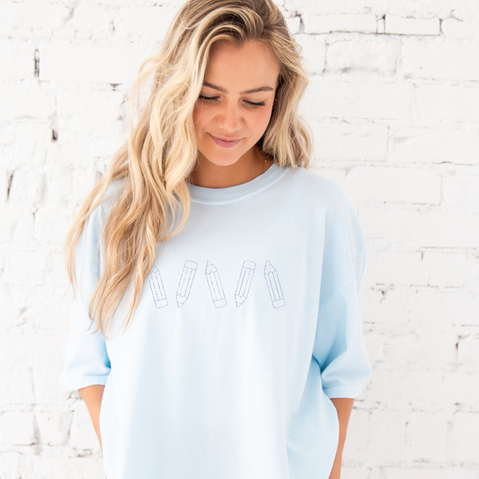 young woman modeling a chambray comfort colors tee with embroidered stitched pencil across the chest in french blue thread