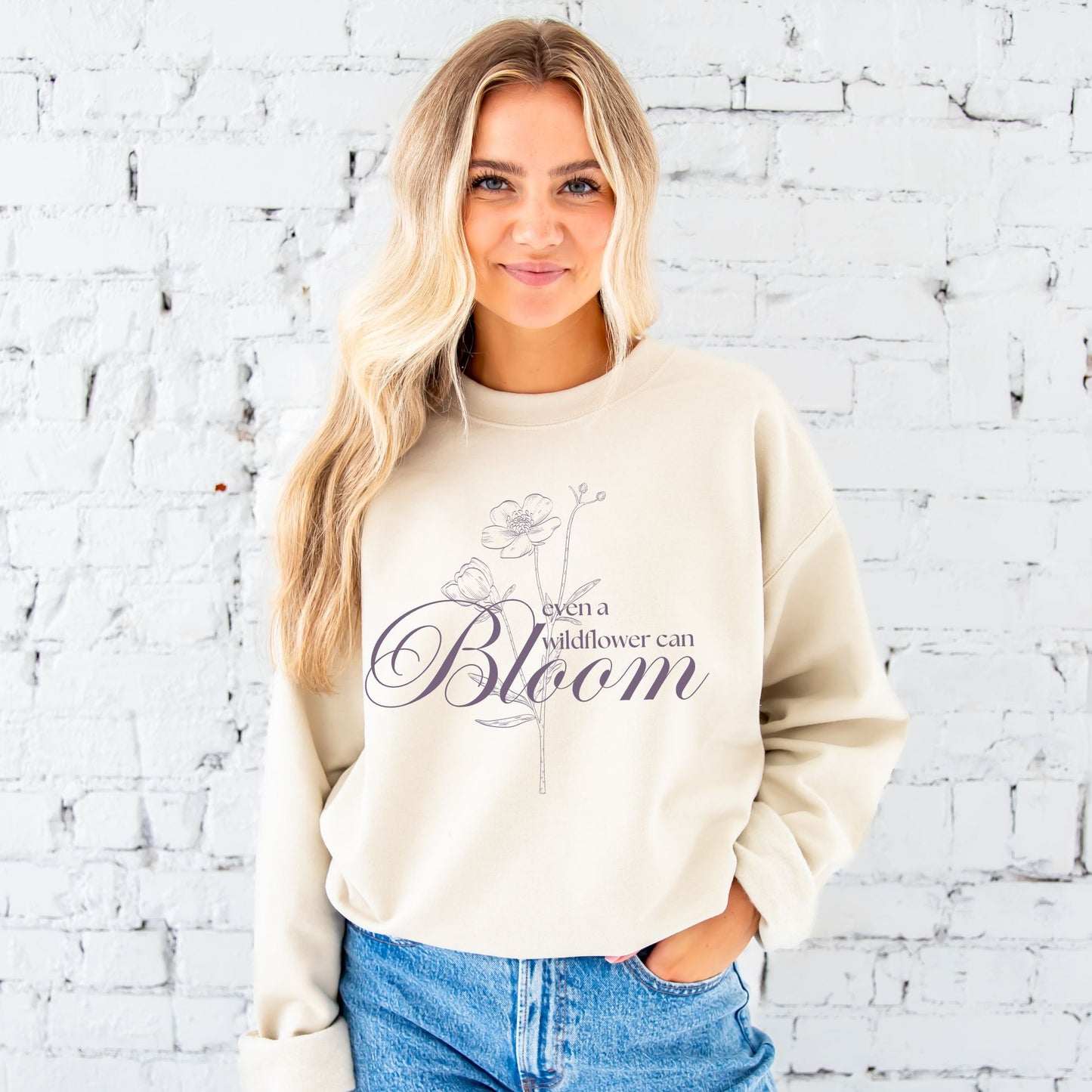 girl wearing a sand sweatshirt with a bridgerton inspired even a wildflower can bloom print