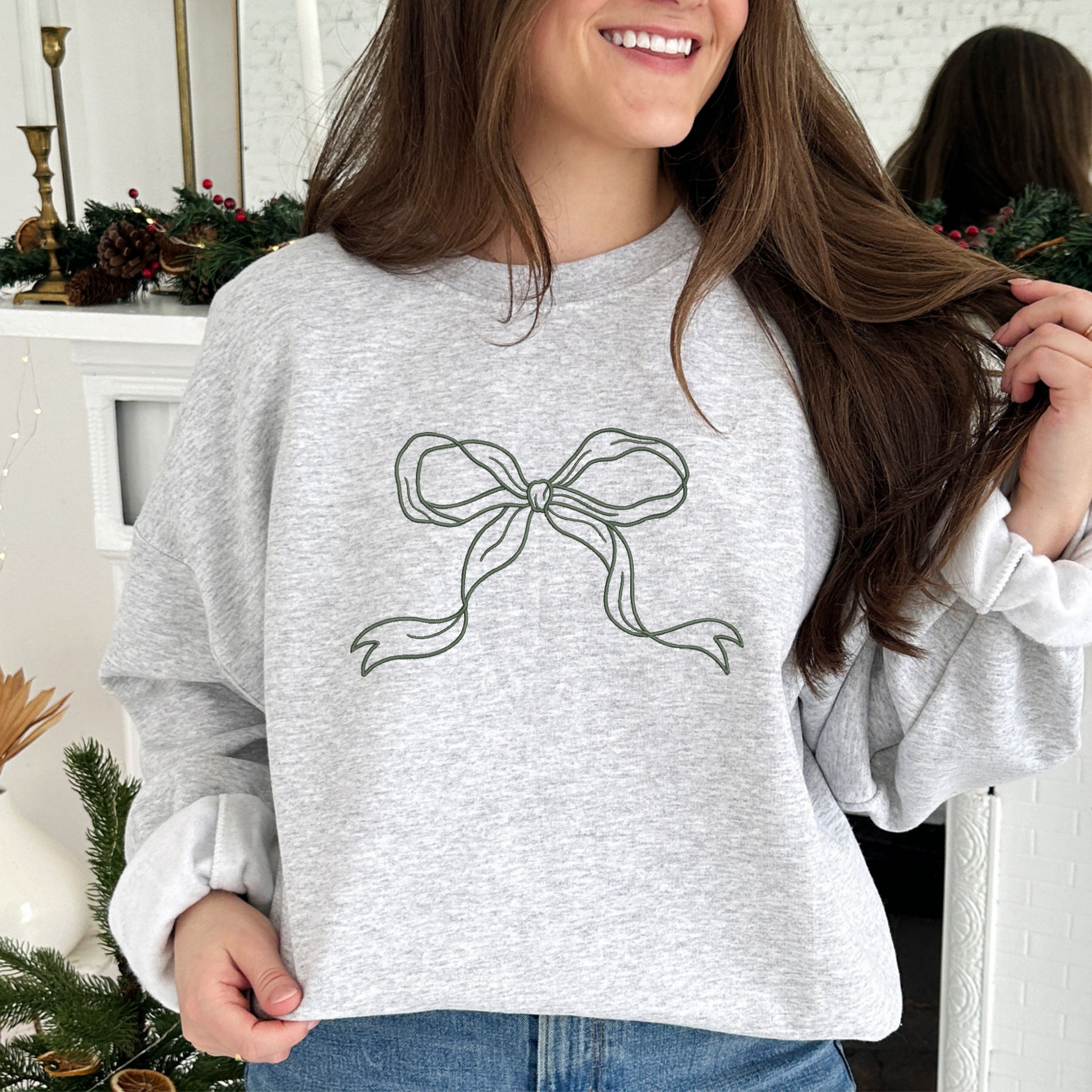 young woman wearing an ash crewneck sweatshirt with a large embroidered ivy green bow across the chest