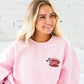 young woman wearing a light pink crewneck sweatshirt with custom embroidered "meet me at Luke's" coffee cup holly design on the left chest